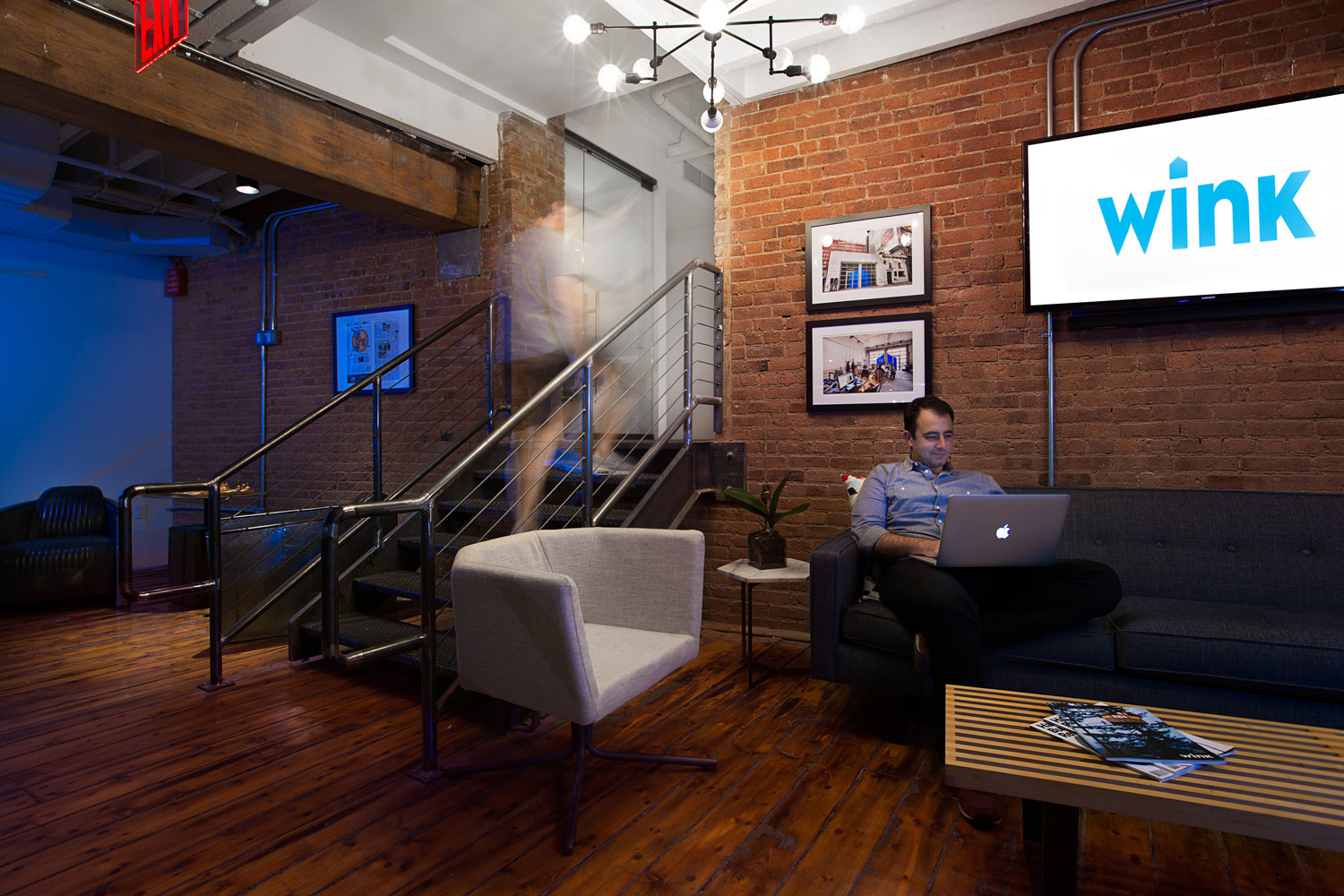 A photo of a Wink employee working on a couch next to a staircase